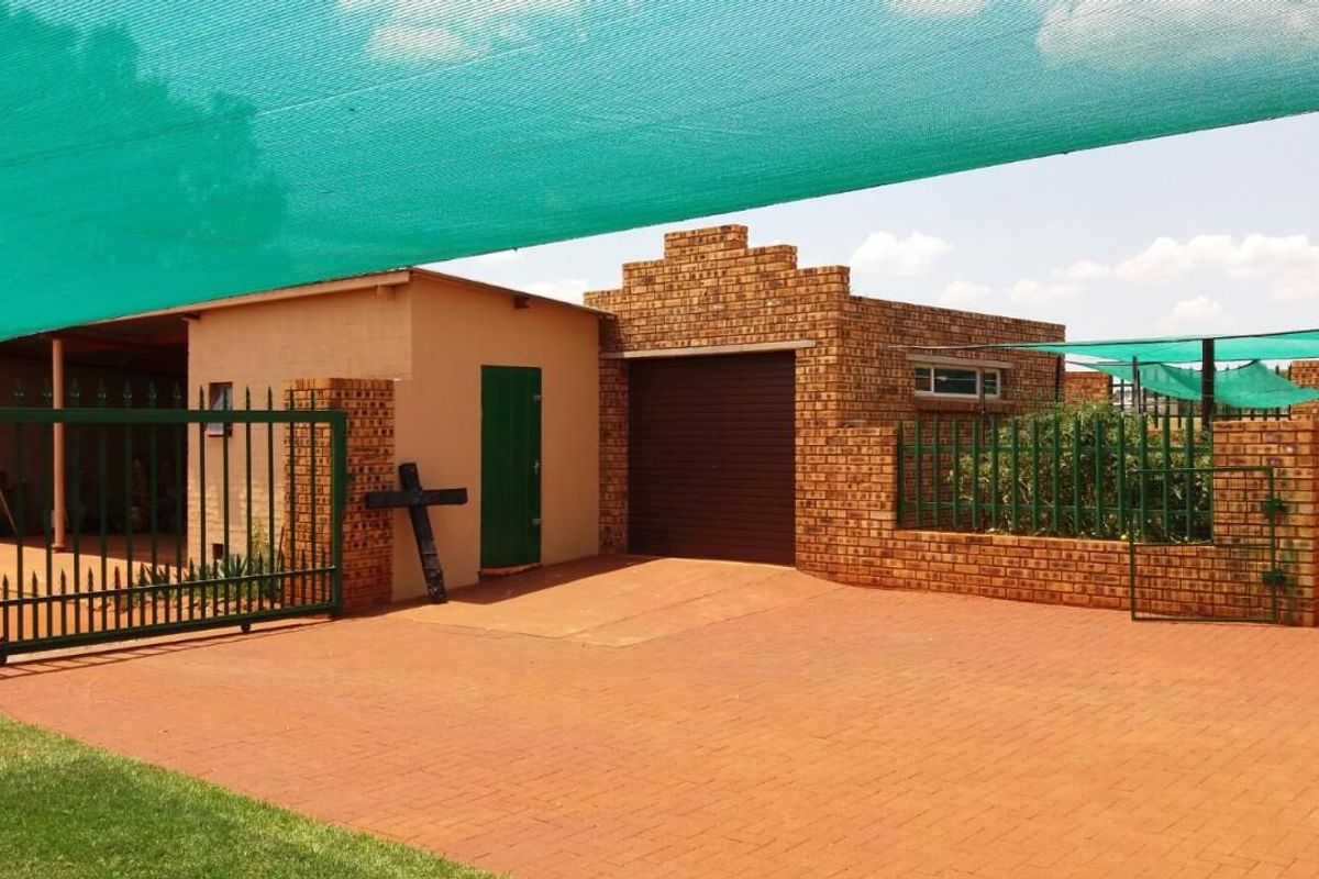 Front exterior view of the property featuring a paved driveway, face brick facade, secure metal gate, and overhead shade cloth canopy.
