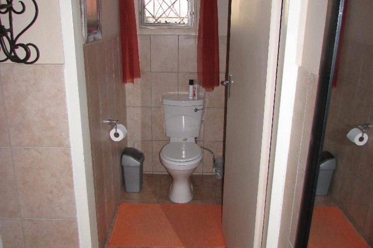 A compact guest bathroom featuring tiled walls and flooring, equipped with a standard toilet and a small window with security bars.