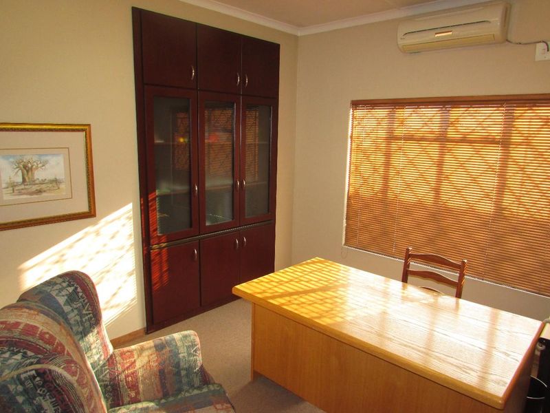 A functional office space featuring built-in dark wood cabinetry, carpeted flooring, a split-system air conditioner, and venetian blinds for light control.