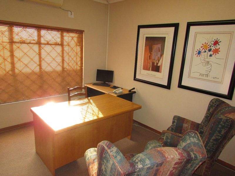 A functional office space featuring carpeted flooring, venetian blinds, and a wall-mounted air conditioning unit.
