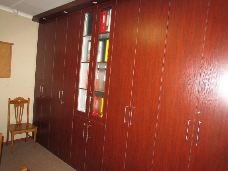 A professional office space featuring extensive floor-to-ceiling built-in wooden cabinetry with integrated glass display sections and recessed lighting.