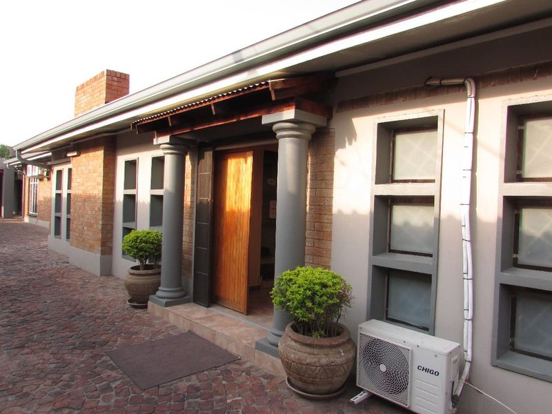 Front entrance of the office building featuring a timber door, decorative columns, brick masonry, and paved exterior walkway.