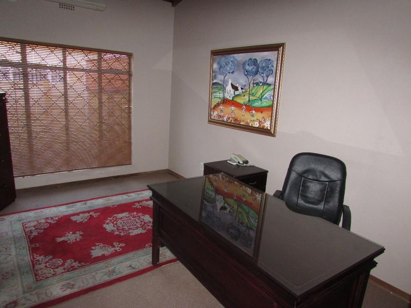A functional office space featuring neutral wall finishes, fitted timber venetian blinds, and a wall-mounted air conditioning unit.