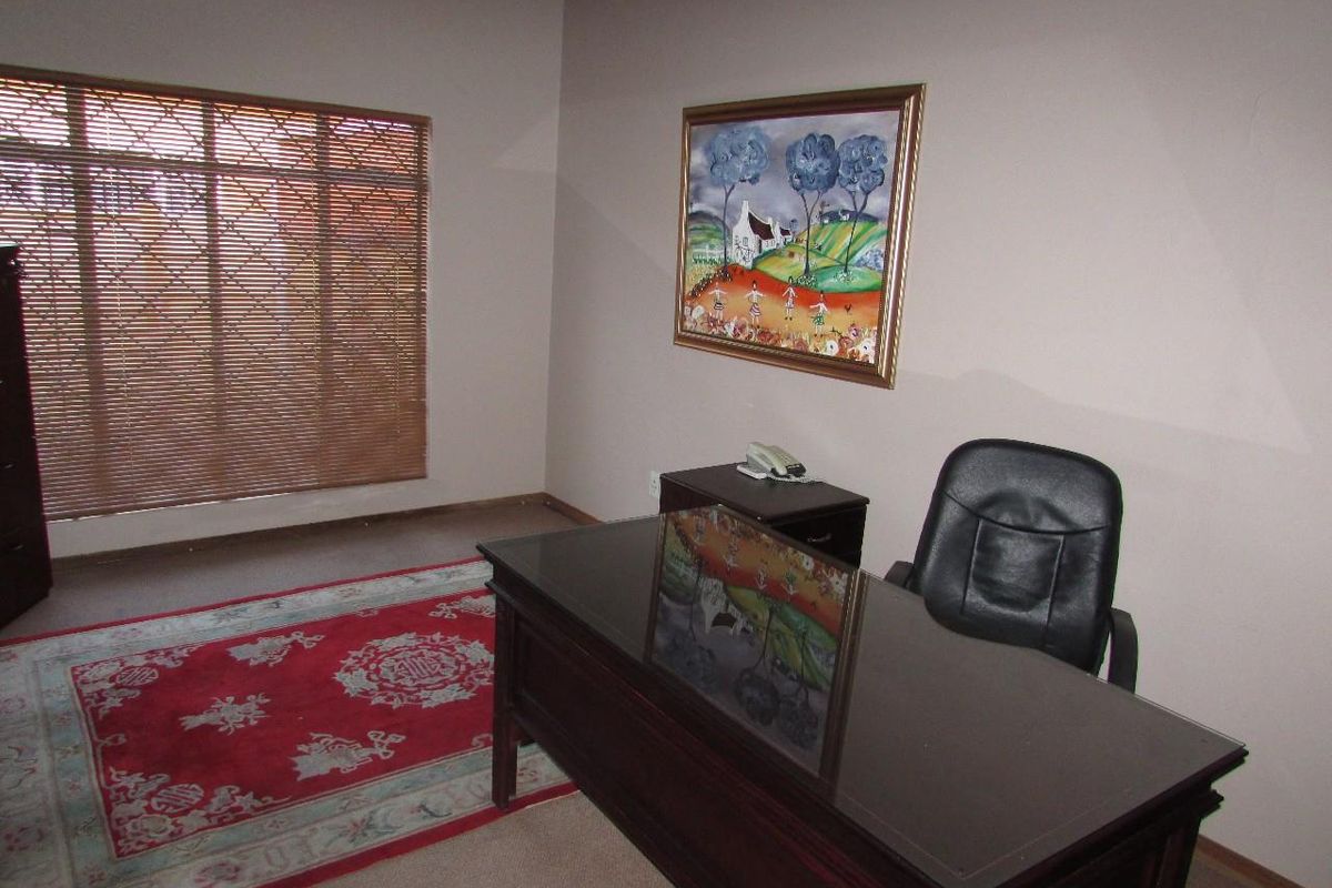 A functional office space featuring neutral wall finishes, fitted timber venetian blinds, and a wall-mounted air conditioning unit.