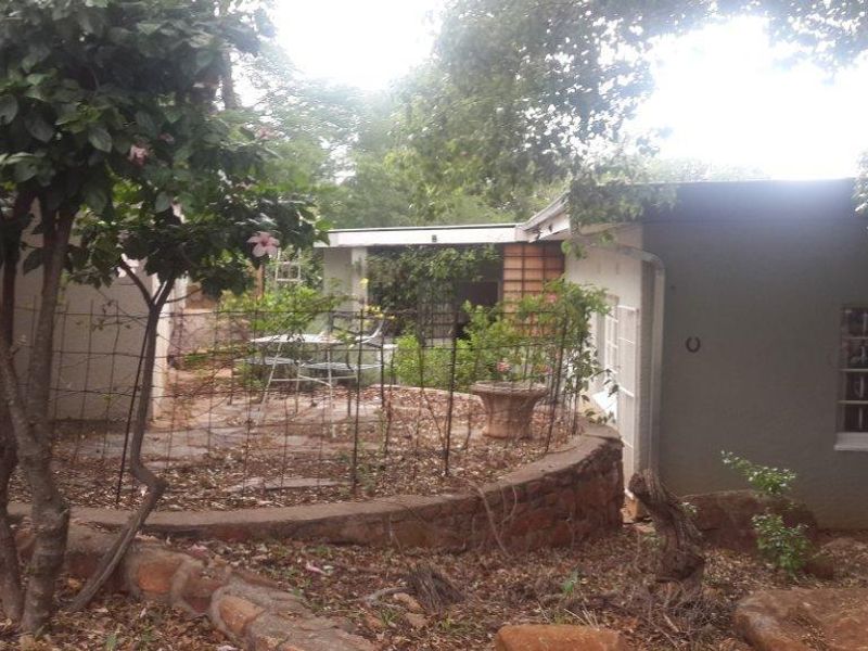 Rear exterior view of the property featuring a stone retaining wall, paved patio area, and established garden surroundings.