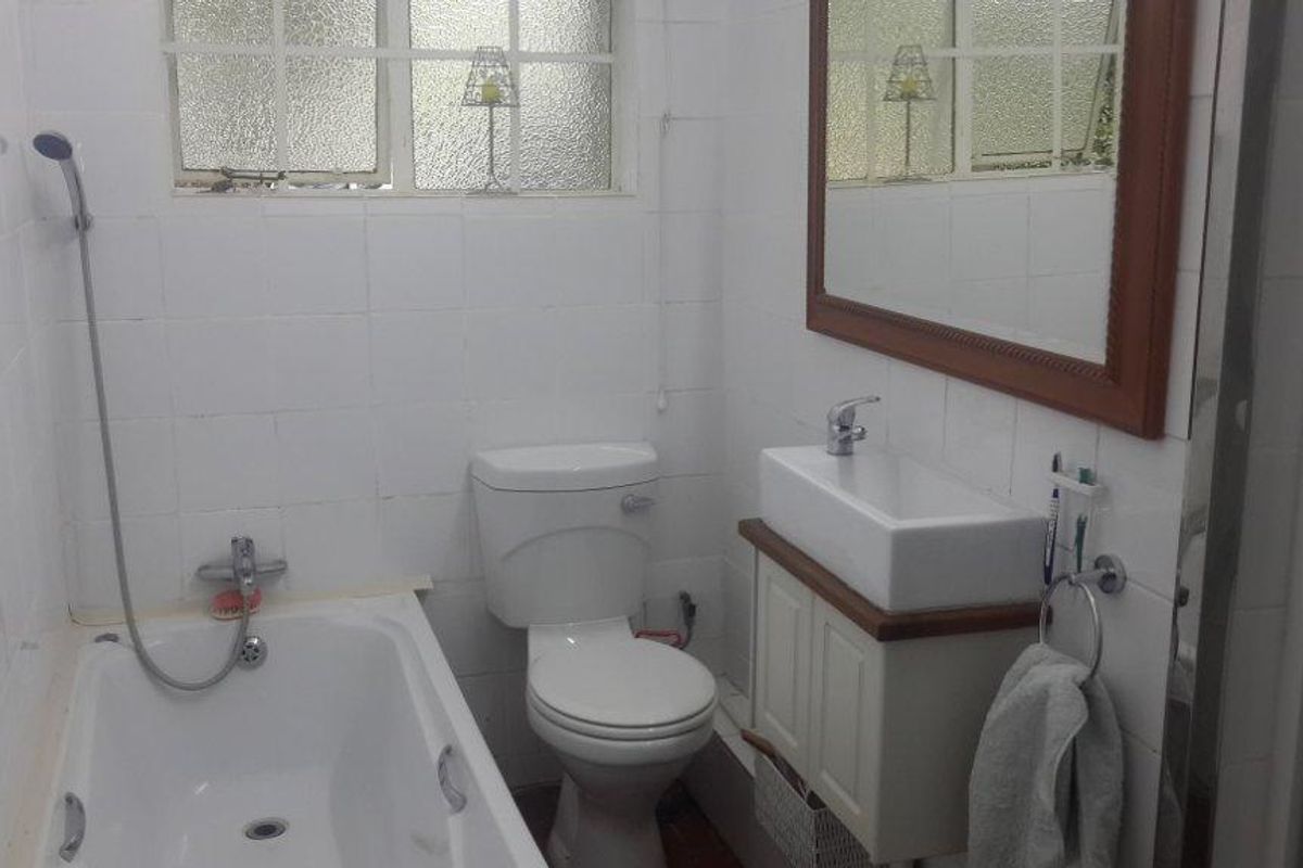 A compact bathroom featuring a bathtub with shower mixer, a white toilet, and a vessel sink set on a vanity cabinet with tiled walls.