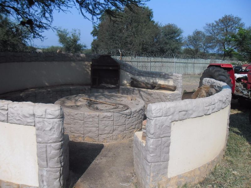 Outdoor entertainment area featuring a circular stone-clad masonry seating arrangement and a built-in braai, set within a rural small holding landscape.