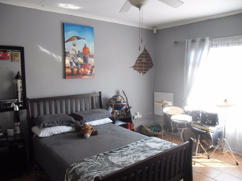 A bedroom featuring tiled flooring, a ceiling fan, and neutral grey walls with some visible plaster damage.