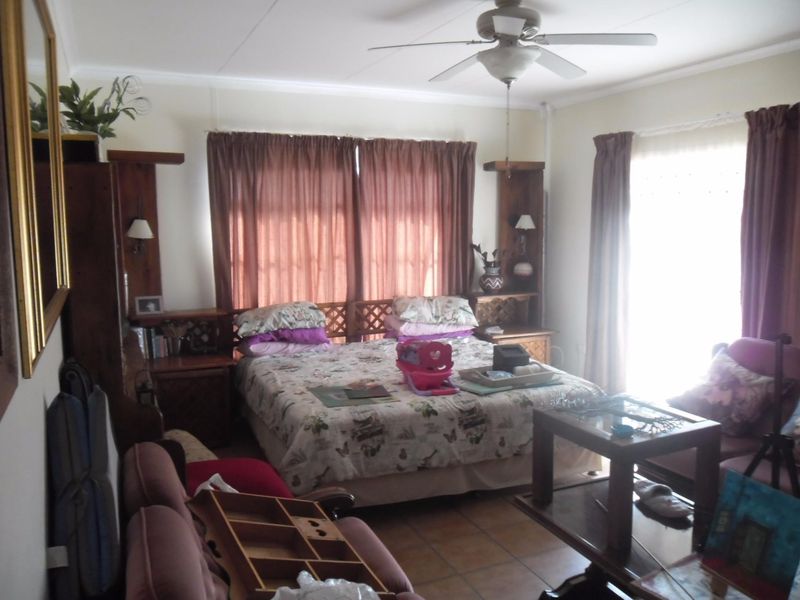 A bedroom featuring tiled flooring, a ceiling fan, and built-in wooden headboard and bedside cabinetry.