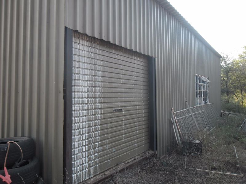 Exterior view of a corrugated metal garage structure featuring a roller shutter door and a damaged window.