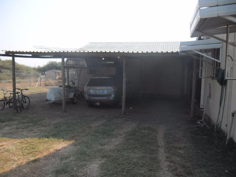 An open-sided carport structure with a corrugated metal roof, providing covered parking space adjacent to the main dwelling.