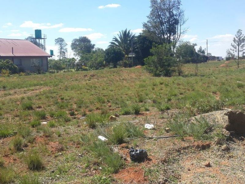 A view of a vacant residential plot featuring natural grass cover and an adjacent structure with a water tank.