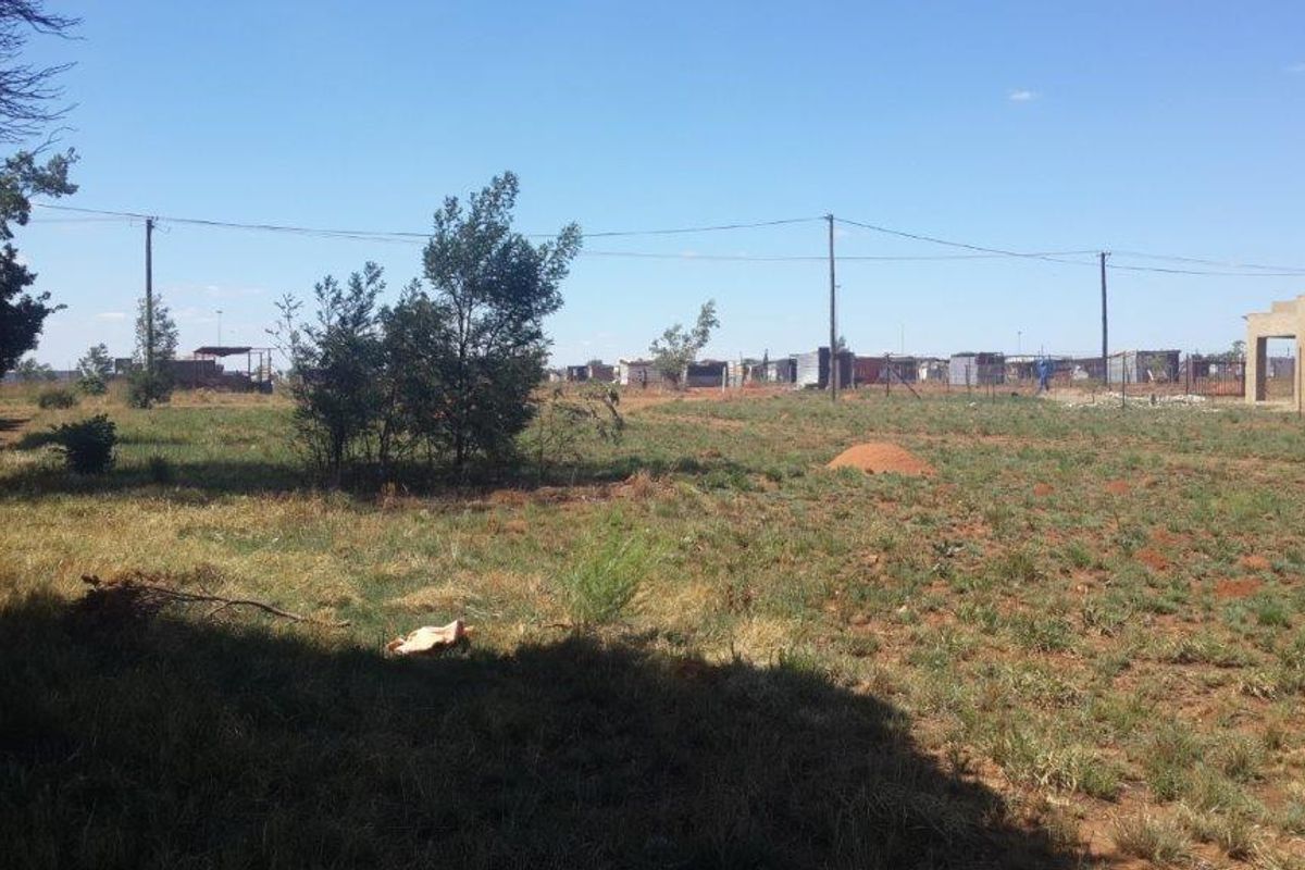 A view of a vacant residential plot featuring natural grass cover, scattered trees, and overhead power lines extending across the property.
