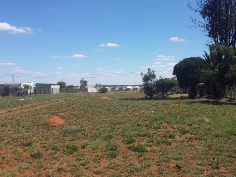 A view of a vacant residential plot featuring natural grass cover, perimeter fencing, and established trees.