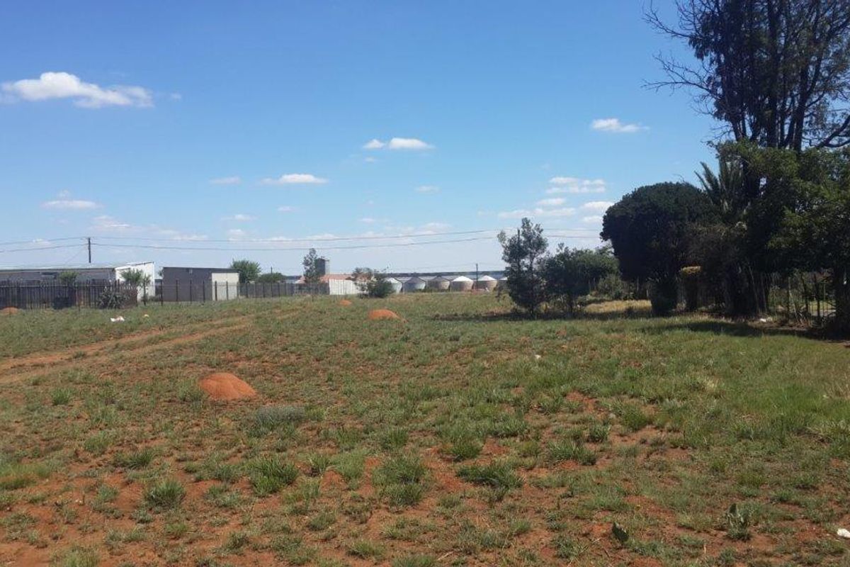 A view of a vacant residential plot featuring natural grass cover, perimeter fencing, and established trees.