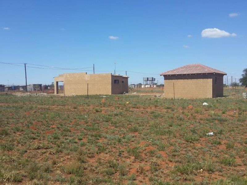 A vacant residential plot featuring two unfinished masonry structures under a clear blue sky, offering potential for further development.
