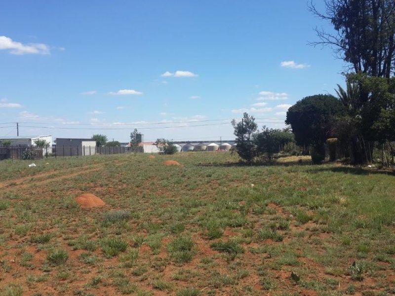 A vacant residential plot featuring natural grass cover, perimeter fencing, and established trees, offering a clear space for potential development.