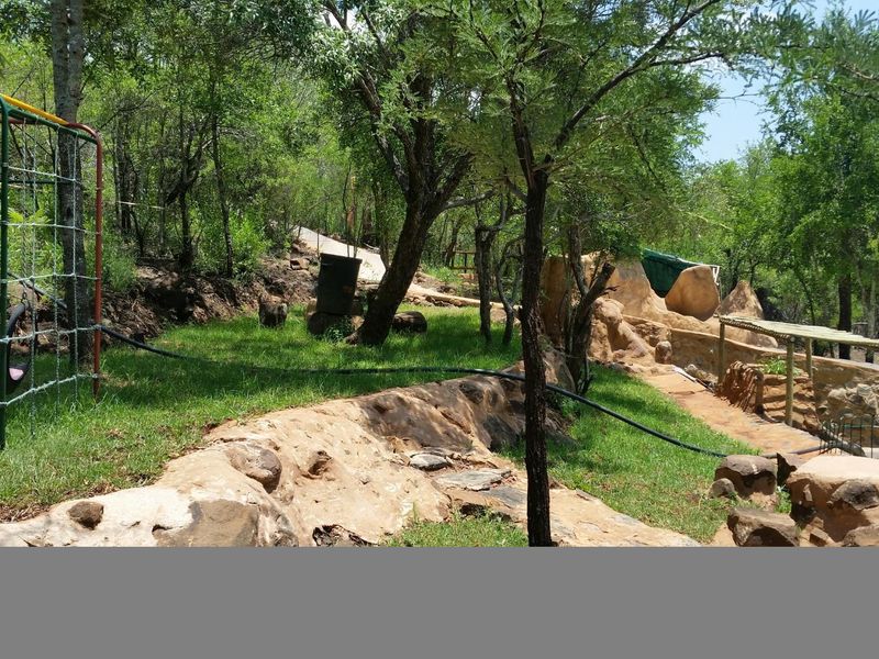 A natural, terraced garden area featuring stone retaining walls, pathways, and mature trees within a rural farm setting.