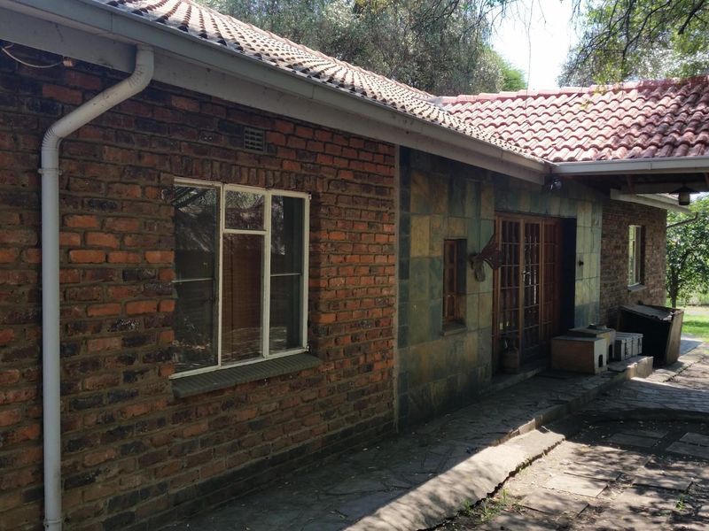 Rear exterior view of a farm-style dwelling featuring exposed brickwork, stone cladding, a tiled roof, and a paved patio area.