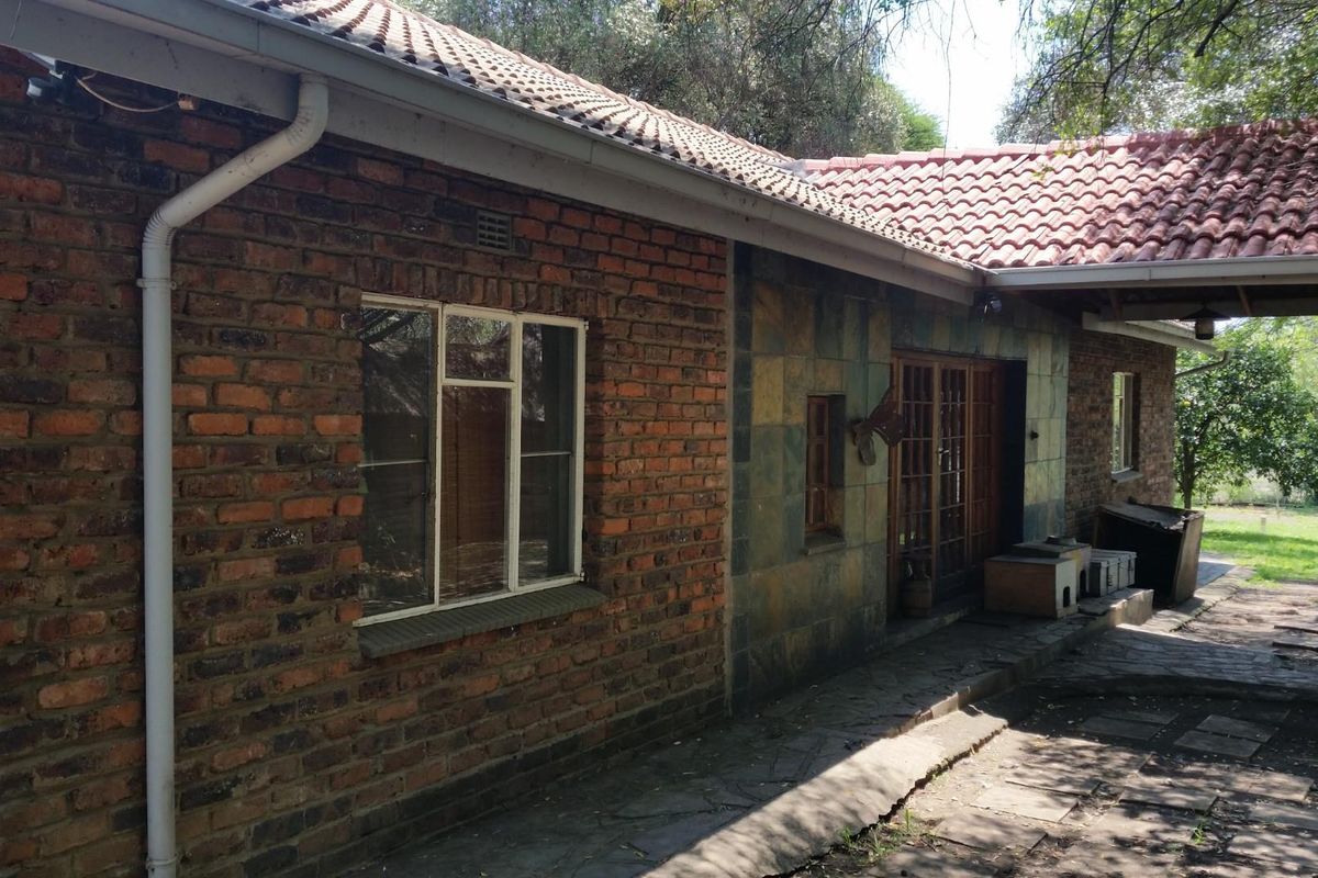 Rear exterior view of a farm-style dwelling featuring exposed brickwork, stone cladding, a tiled roof, and a paved patio area.