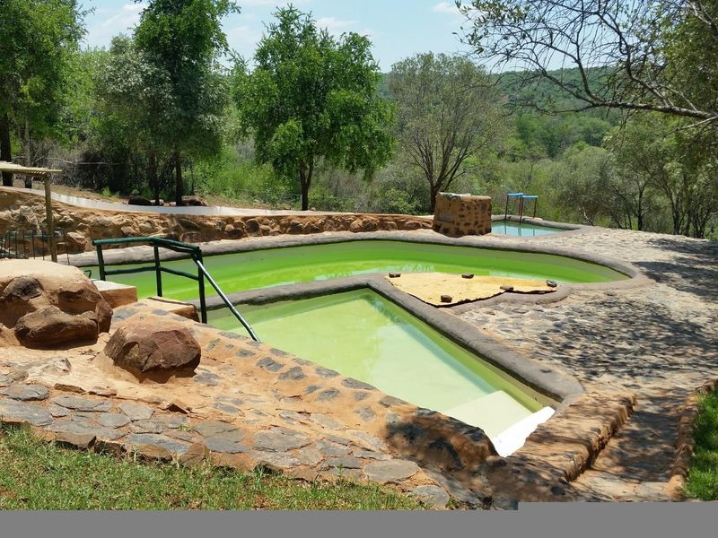 Outdoor swimming pool area featuring stone-clad construction and natural stone paving, set within a rural landscape with mature trees.