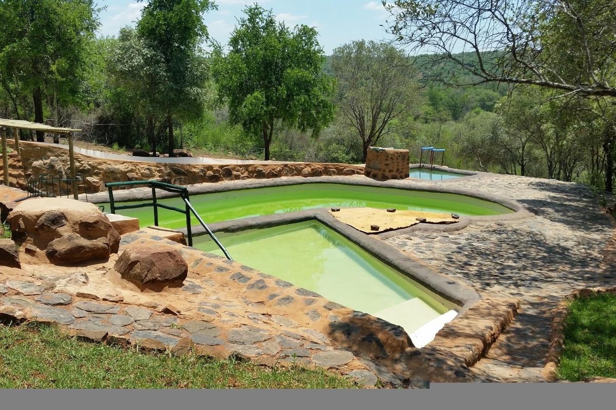 Outdoor swimming pool area featuring stone-clad construction and natural stone paving, set within a rural landscape with mature trees.