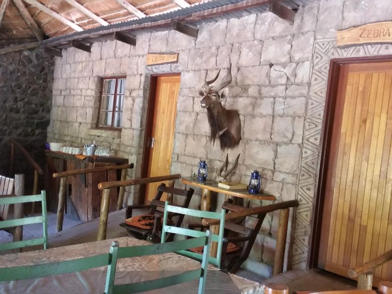 Rustic covered patio area featuring stone masonry walls, exposed timber rafters, and a thatched roof, providing a traditional farm-style outdoor living space.