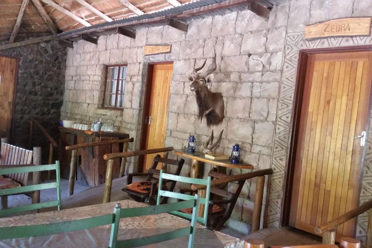 Rustic covered patio area featuring stone masonry walls, exposed timber rafters, and a thatched roof, providing a traditional farm-style outdoor living space.