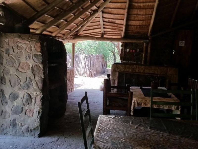 Rustic outdoor patio area featuring a traditional thatched roof, stone masonry fireplace, and exposed timber rafters, perfect for relaxed farm-style entertaining.