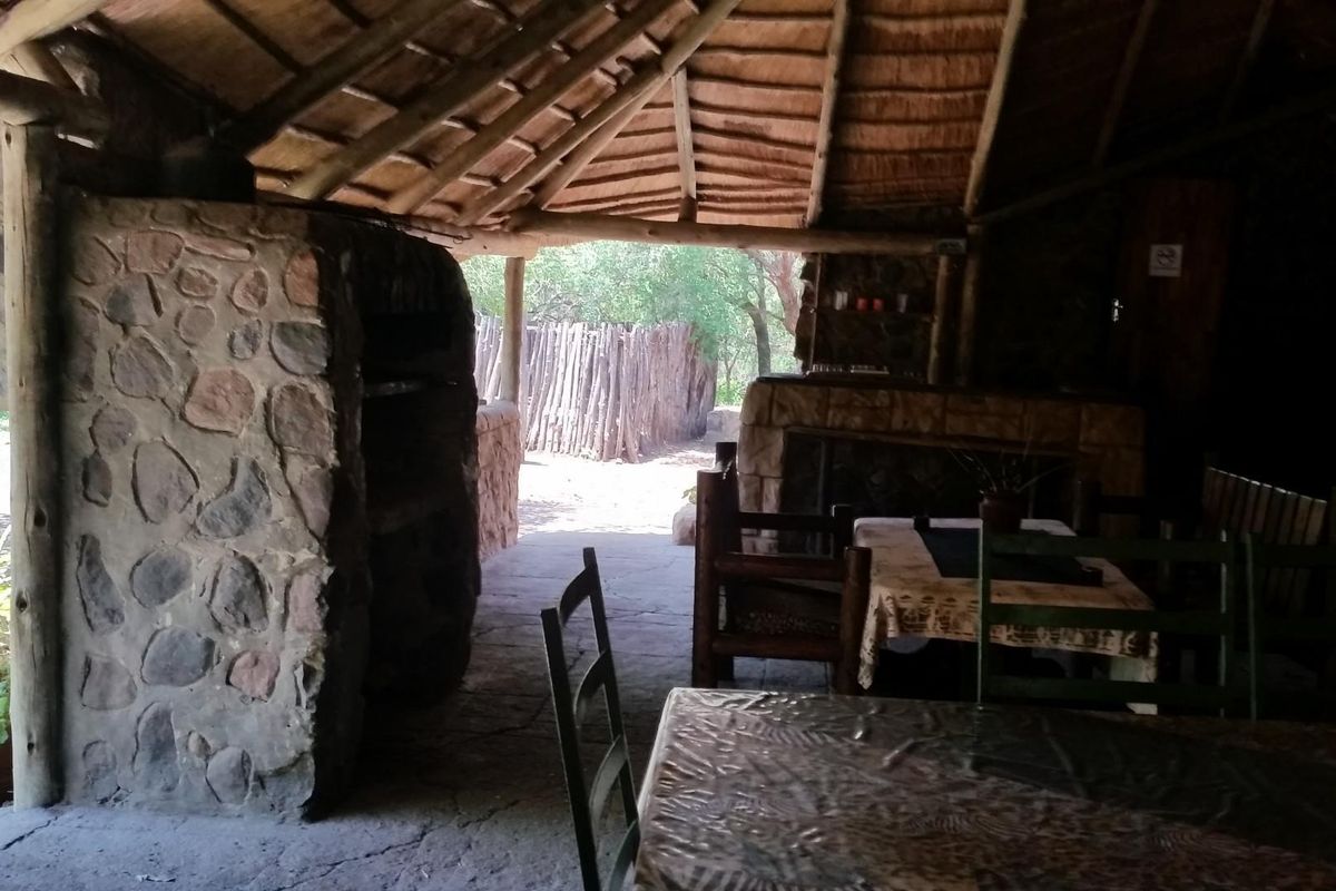 Rustic outdoor patio area featuring a traditional thatched roof, stone masonry fireplace, and exposed timber rafters, perfect for relaxed farm-style entertaining.