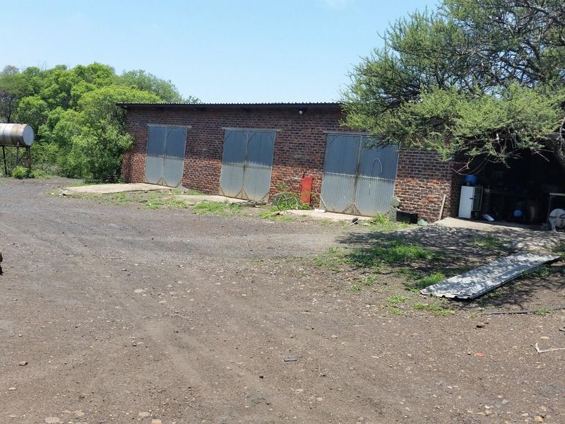 A rustic farm outbuilding featuring multiple metal garage doors, brick construction, and an adjacent water storage tank on a dirt yard.