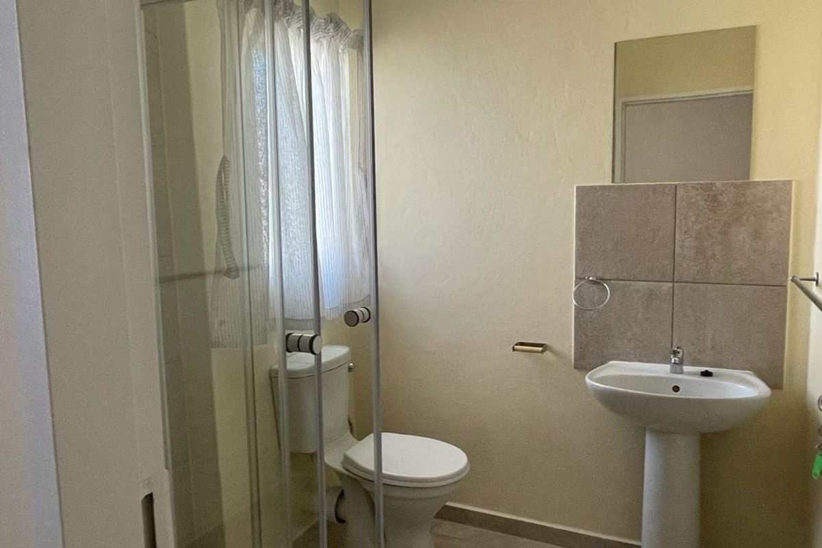 A functional bathroom featuring a pedestal basin, a glass-enclosed shower, and a standard toilet with neutral wall finishes.