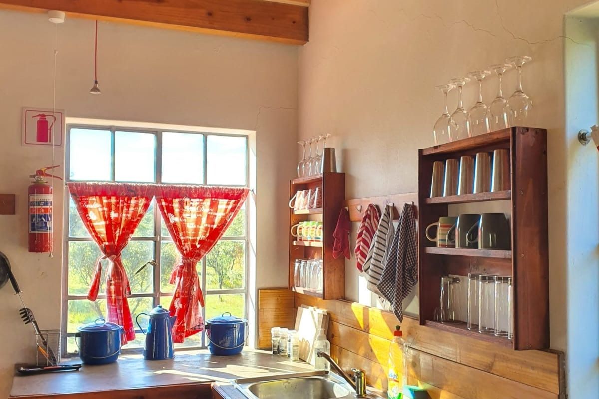 A rustic kitchen area featuring wooden cabinetry, a double stainless steel sink, exposed timber ceiling beams, and a window with natural light.