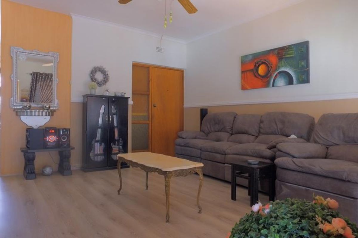 A living room featuring light wood-look flooring, a ceiling fan, and a wooden door with glass paneling.
