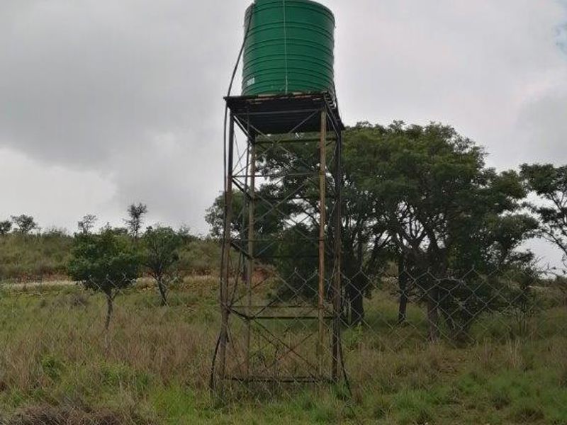 An elevated water storage tank mounted on a metal support structure located within a fenced area on the small holding.