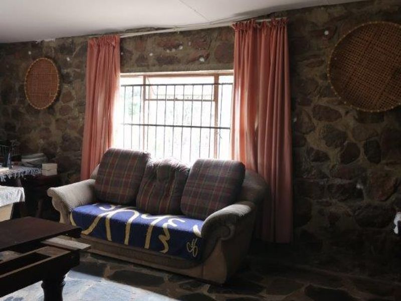 Rustic living room featuring natural stone wall cladding, traditional flagstone flooring, and a window fitted with security bars.