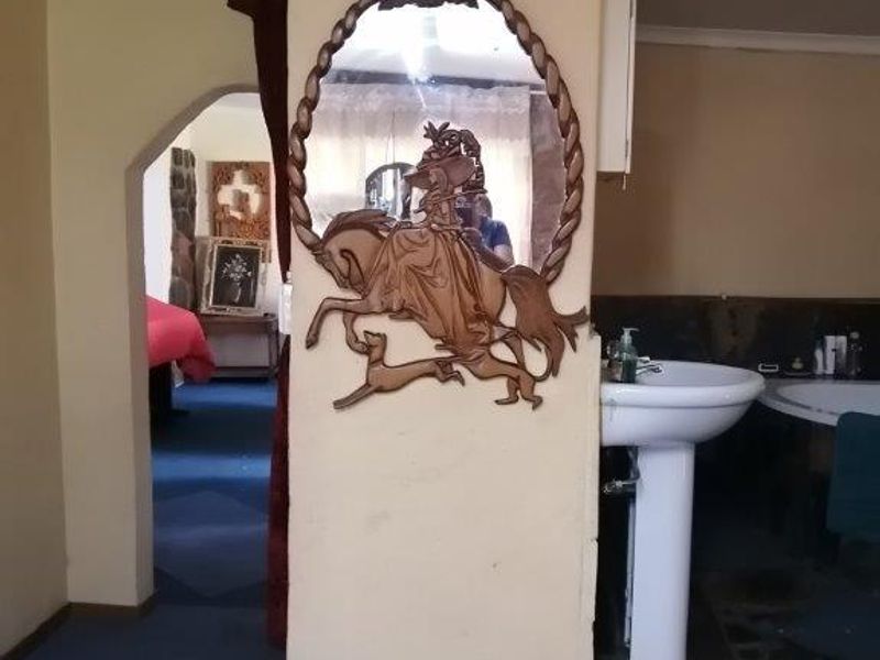 A bathroom area featuring a pedestal basin and an archway leading to an adjacent room, showcasing dated finishes and flooring.
