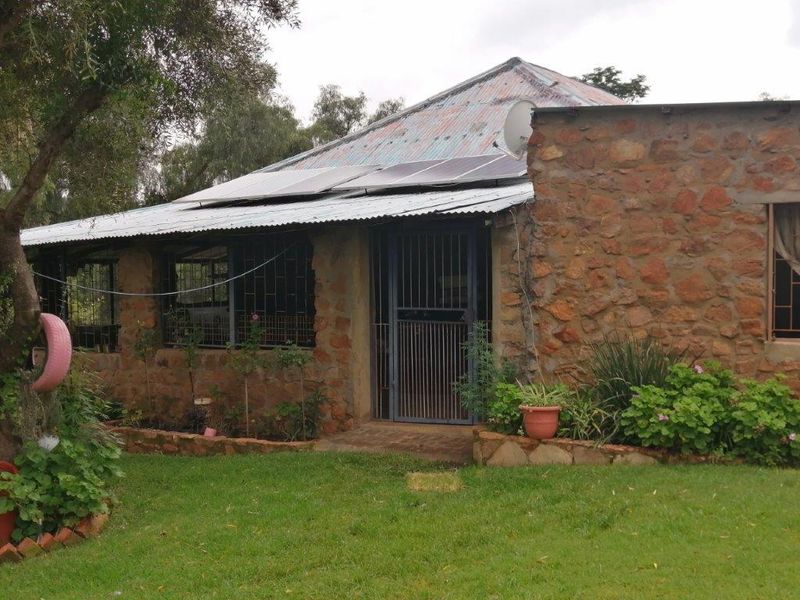 Rear view of a stone-clad small holding dwelling featuring a corrugated metal roof with installed solar panels and security fixtures.