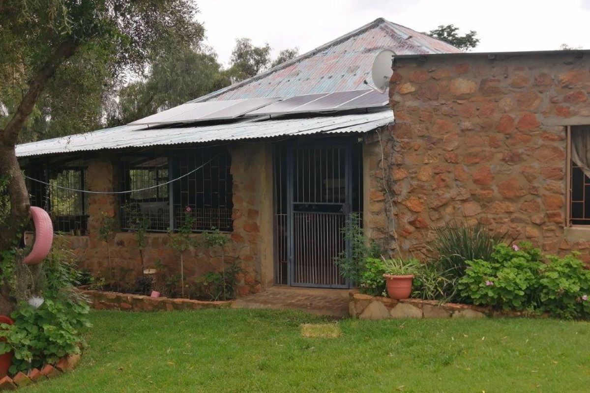 Rear view of a stone-clad small holding dwelling featuring a corrugated metal roof with installed solar panels and security fixtures.