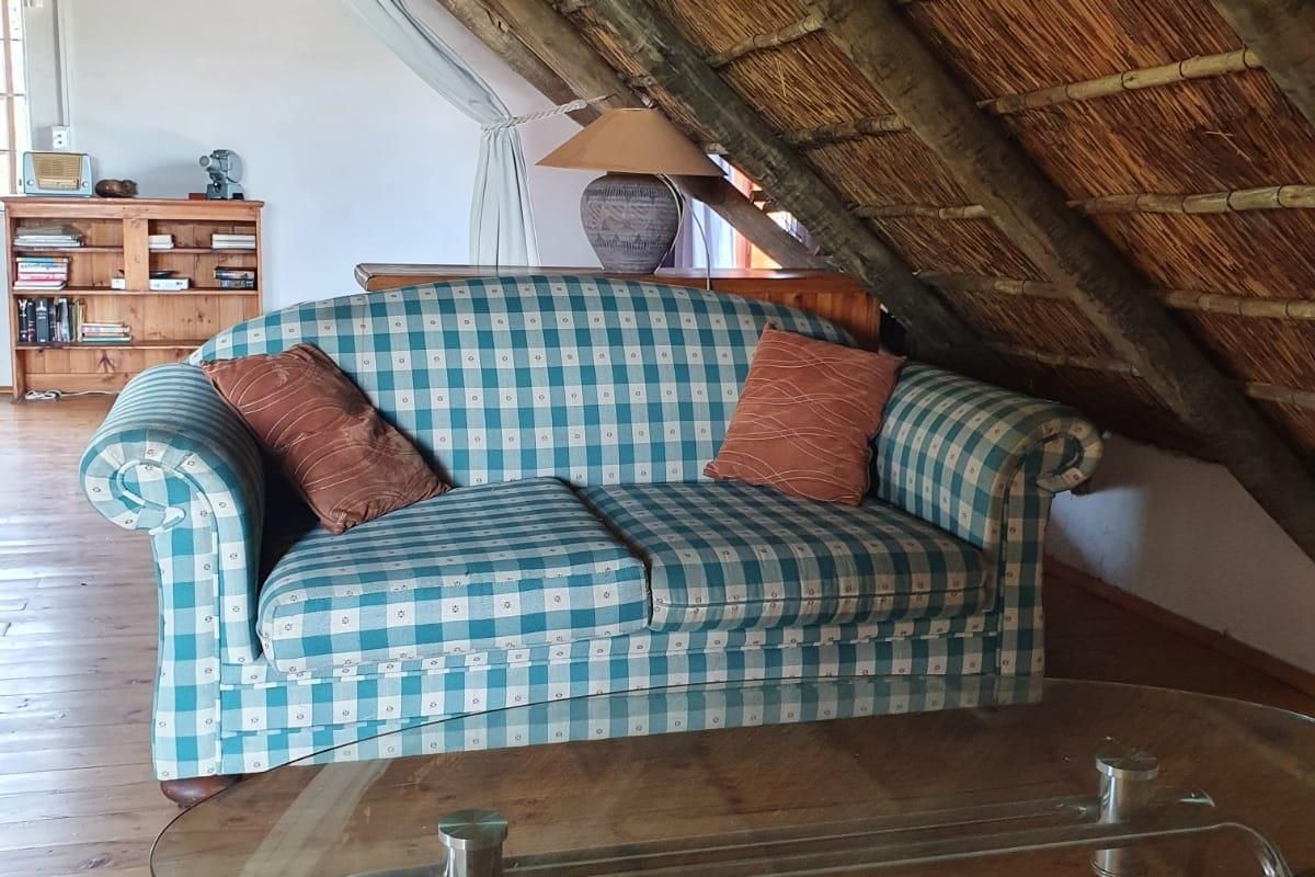 A cozy living area featuring a unique pitched thatch roof, exposed timber rafters, and warm wooden flooring, creating a rustic and inviting atmosphere.