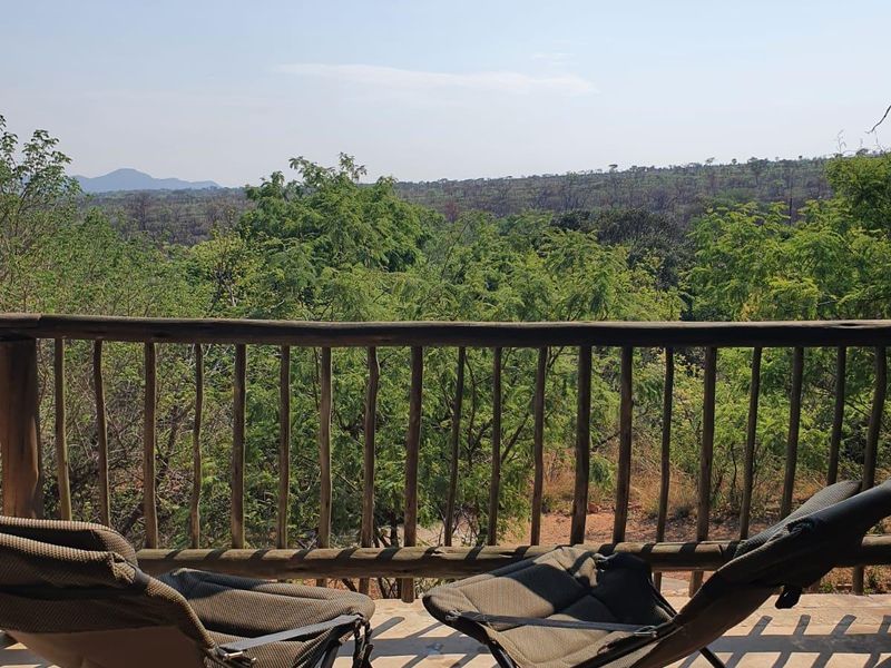 An elevated balcony featuring a rustic wooden balustrade and concrete flooring, offering expansive views of the surrounding natural landscape.