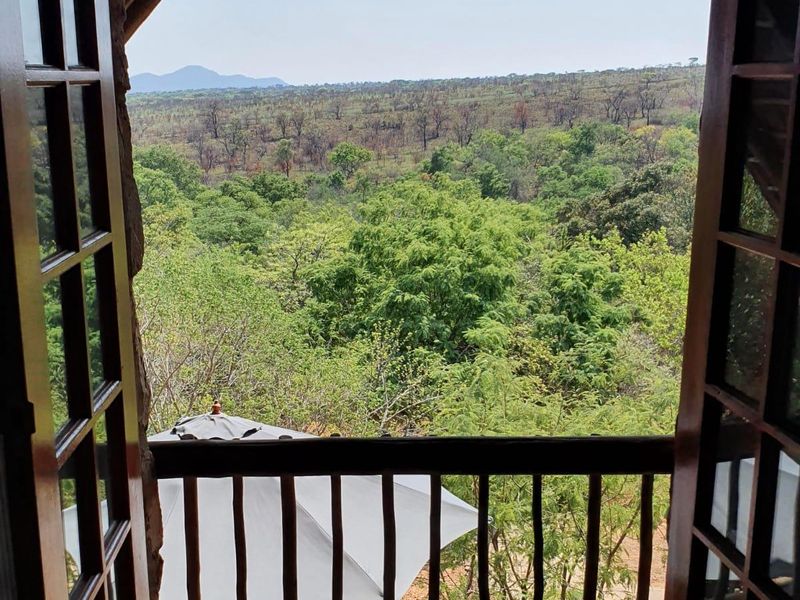 A rustic wooden balcony featuring a timber balustrade and French doors, offering expansive views of the surrounding natural landscape.