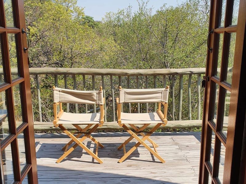A wooden balcony deck featuring a rustic timber balustrade and double french doors, offering an elevated view of the surrounding natural landscape.