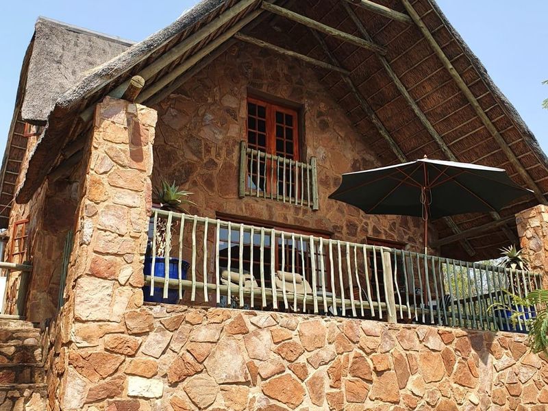 A charming double-story stone-clad house featuring a traditional thatched roof, a wooden balcony, and an external stone staircase.