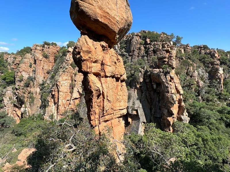 A scenic view of a prominent natural rock formation set against a rugged landscape with native vegetation.