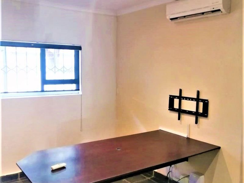 A functional office space featuring tiled flooring, recessed downlighting, a wall-mounted air conditioning unit, and a built-in desk surface.