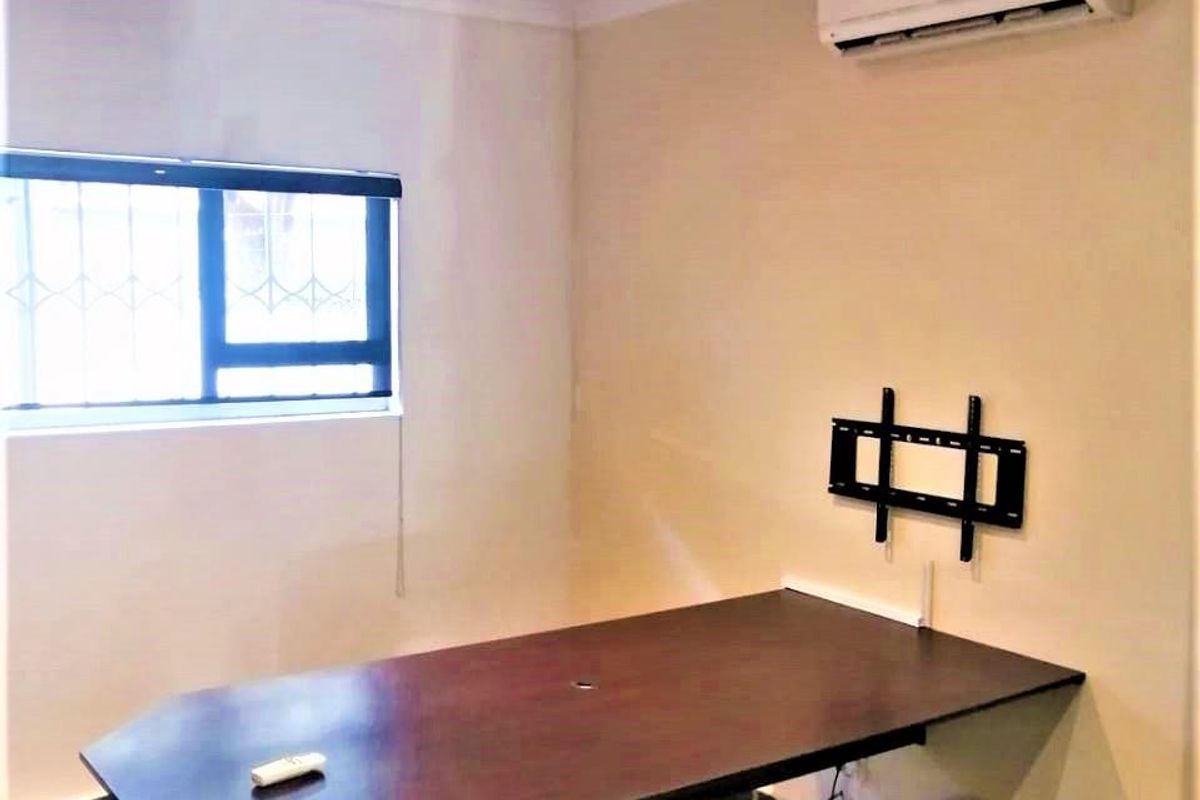 A functional office space featuring tiled flooring, recessed downlighting, a wall-mounted air conditioning unit, and a built-in desk surface.