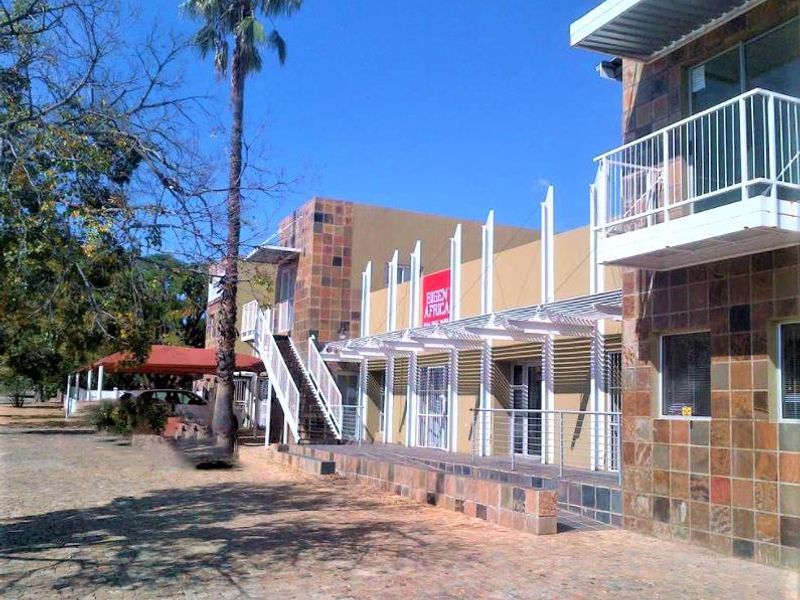 Exterior view of a commercial building featuring stone cladding, a metal staircase, and a covered balcony area with a paved courtyard.