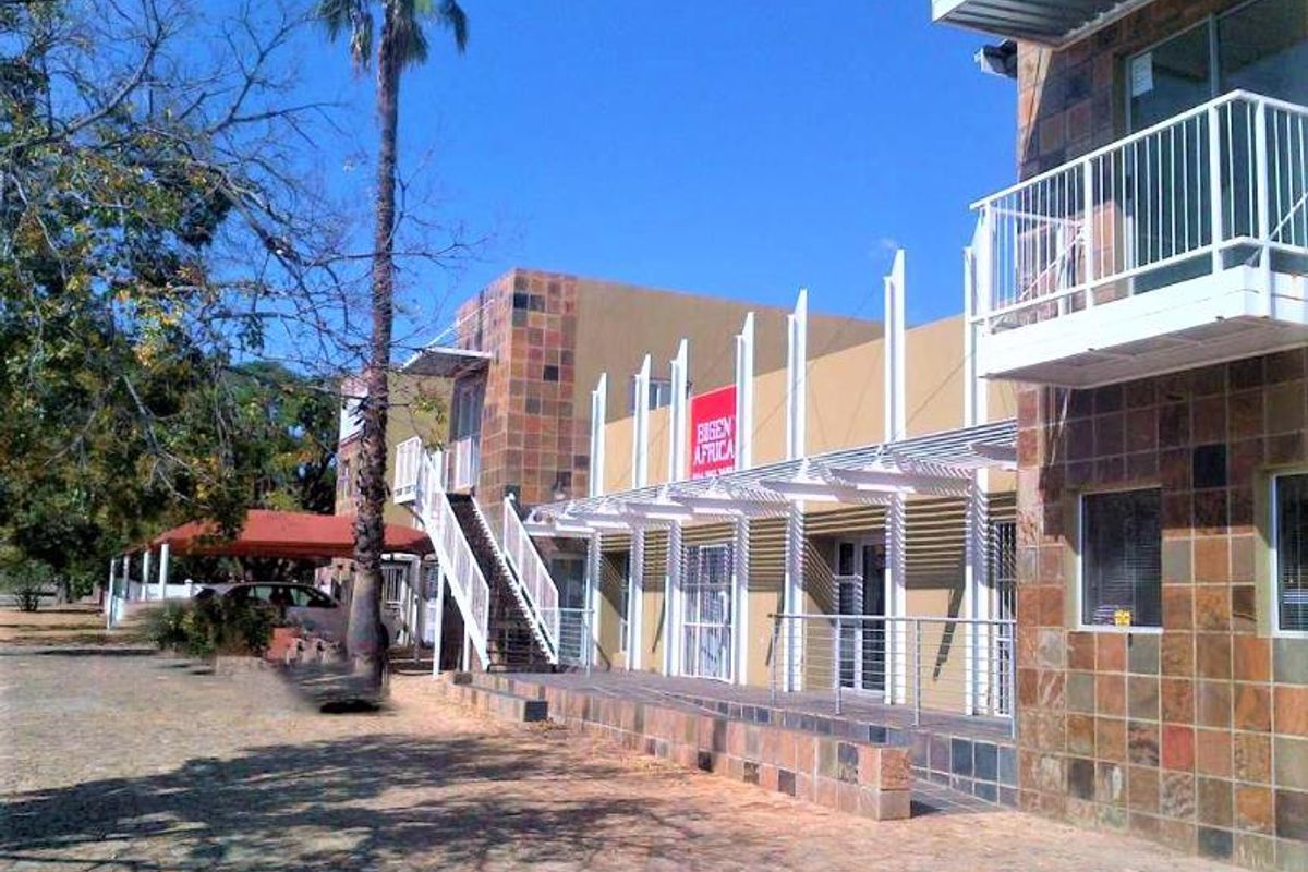 Exterior view of a commercial building featuring stone cladding, a metal staircase, and a covered balcony area with a paved courtyard.