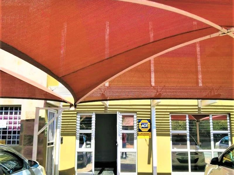 Commercial property entrance featuring a paved driveway, shade sail structure, and secure aluminium framed glass doors and windows.